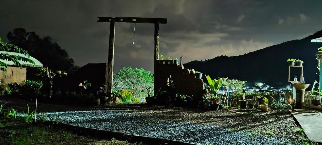 A nighttime view of a rural area with a wooden structure, possibly a gate or entrance, surrounded by greenery and plants.