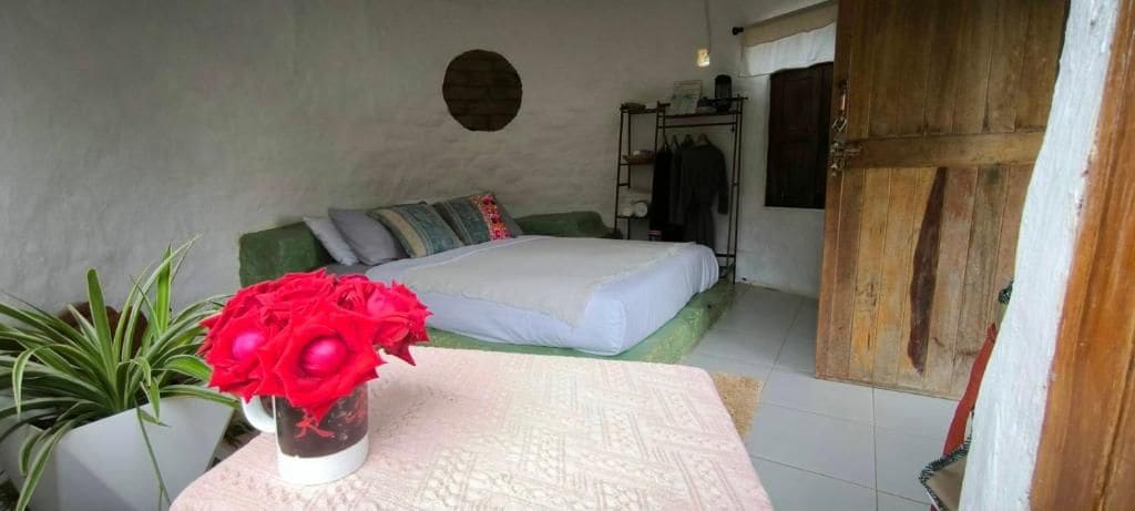 Ein Schlafzimmer mit einem Bett, einem Nachttisch mit einer Vase roter Blumen, einem Kleiderschrank und einer Tür.