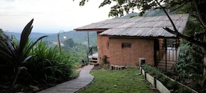 A rustic house with a thatched roof, a paved pathway leading to the entrance, and a view of the surrounding landscape.