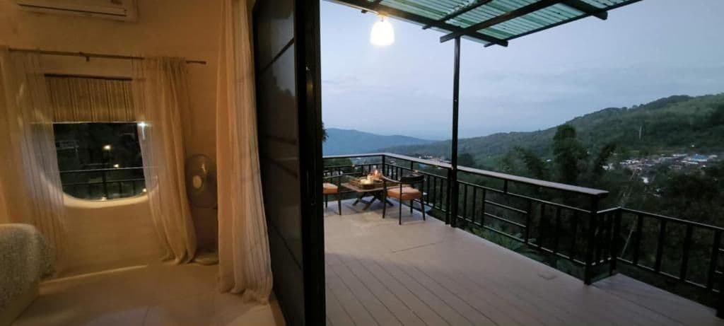 Un balcón con mesa y sillas, vistas al paisaje y una ventana con cortinas.
