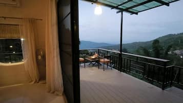 Un balcón con mesa y sillas, vistas al paisaje y una ventana con cortinas.