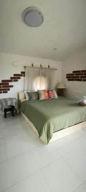 A bedroom with a bed, a bedside table, a lamp, and a window with curtains.