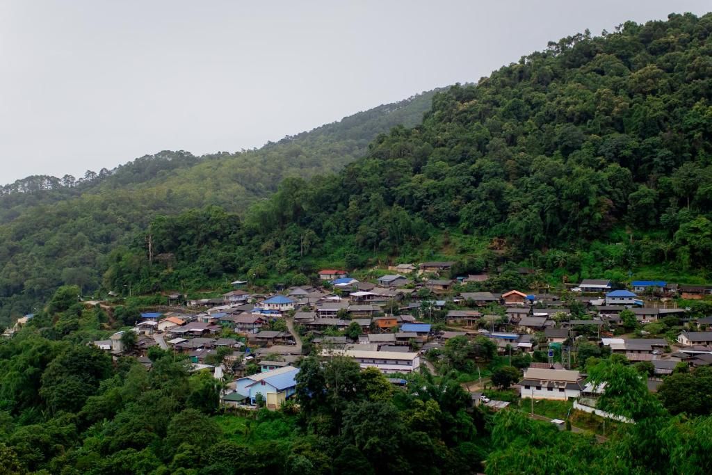 A hillside village with traditional houses, dense greenery, and a hilly backdrop.