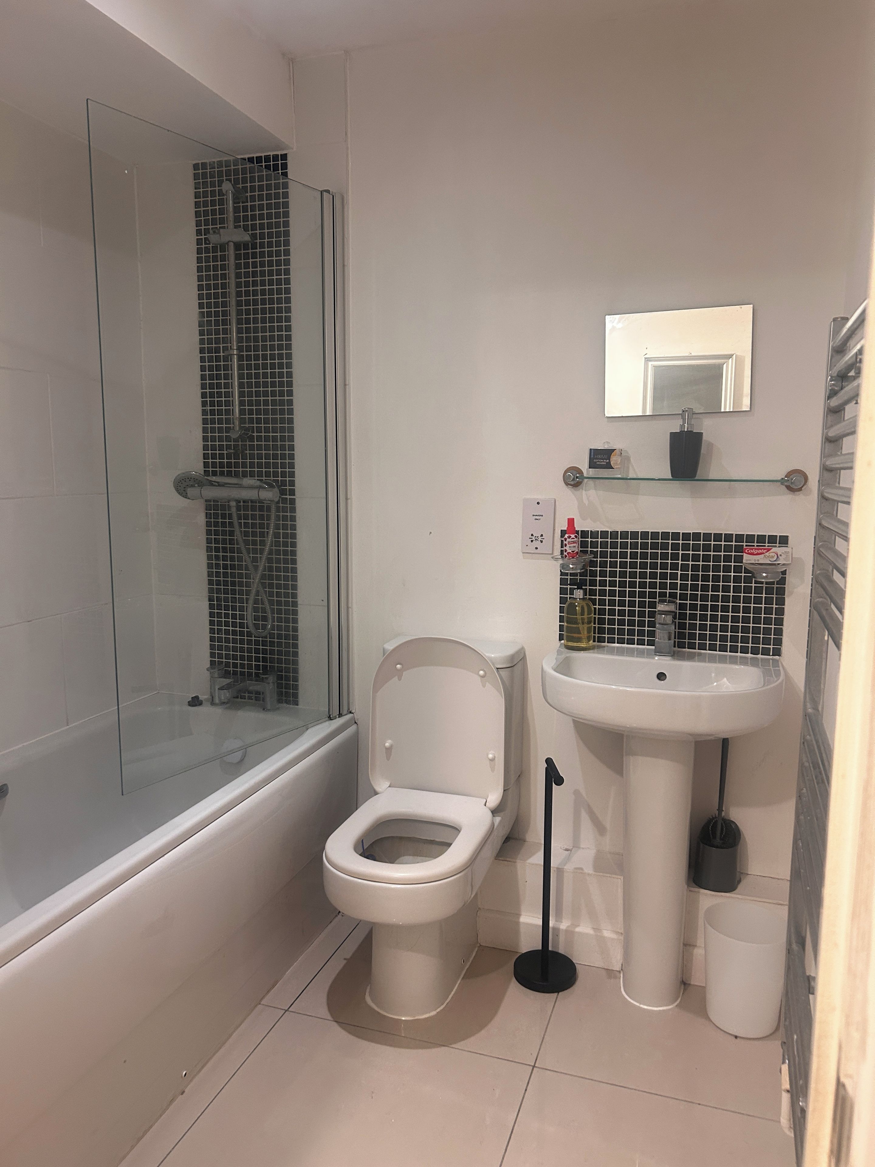 A bathroom with a glass-enclosed shower, a white toilet, a pedestal sink, and a mirror above the sink.