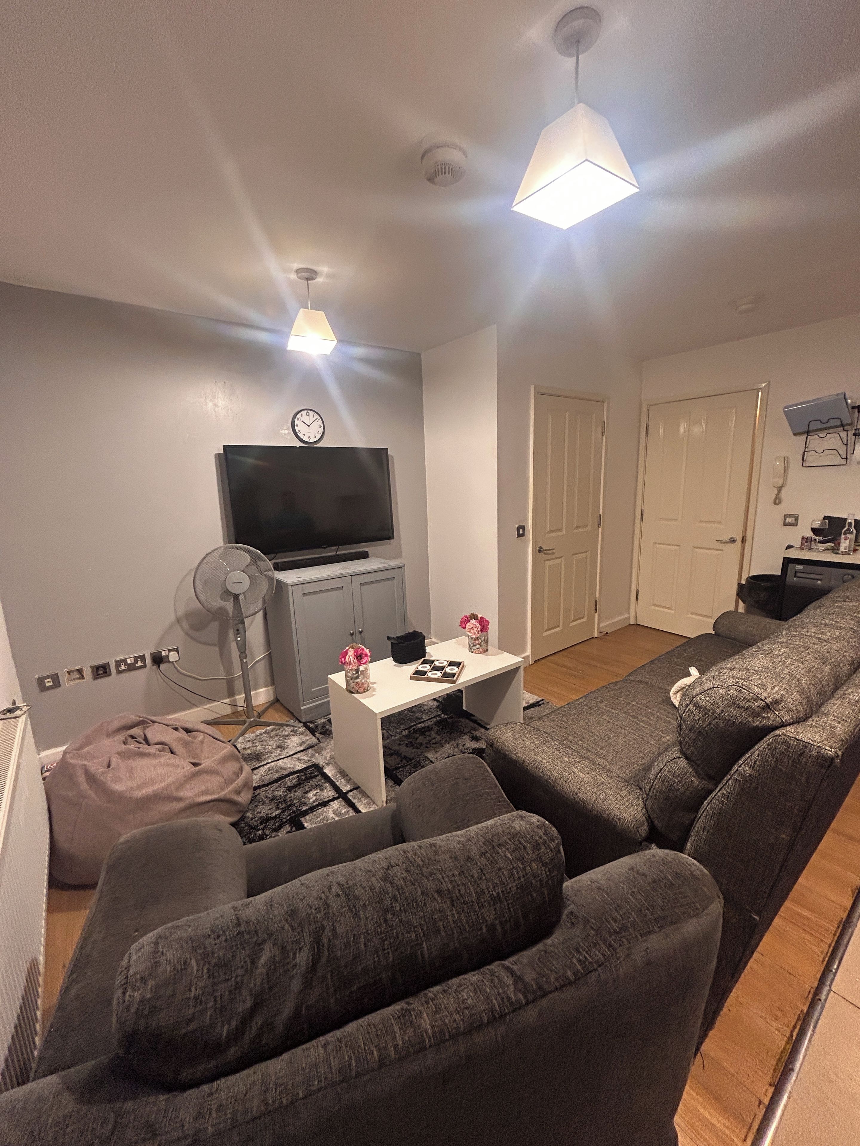 A living room with a sofa, a TV, a small table with flowers, and a fan.
