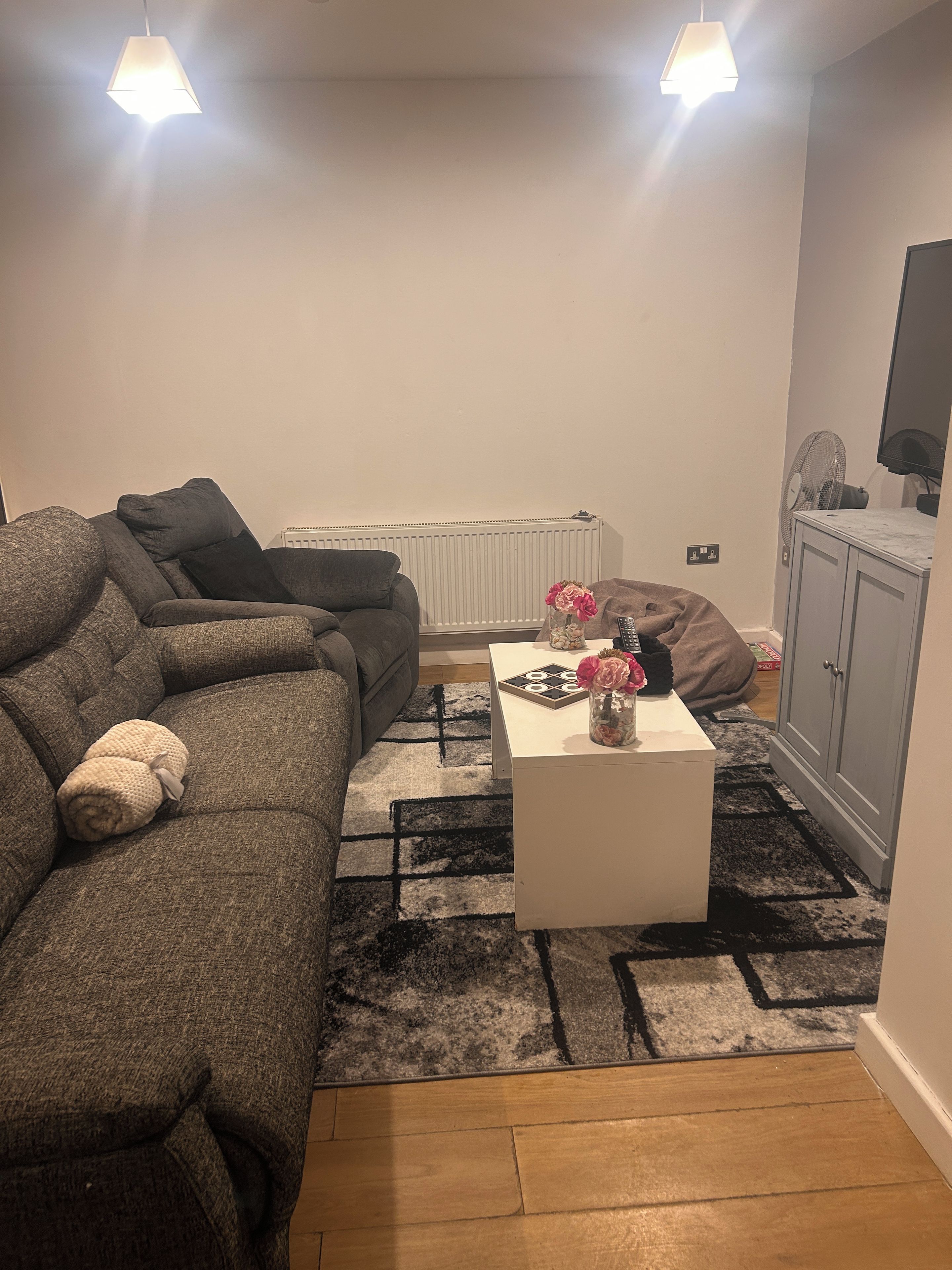 Ein Wohnzimmer mit einer Couch, einem Couchtisch mit einer Vase, einem Heizkörper und einem Schrank.