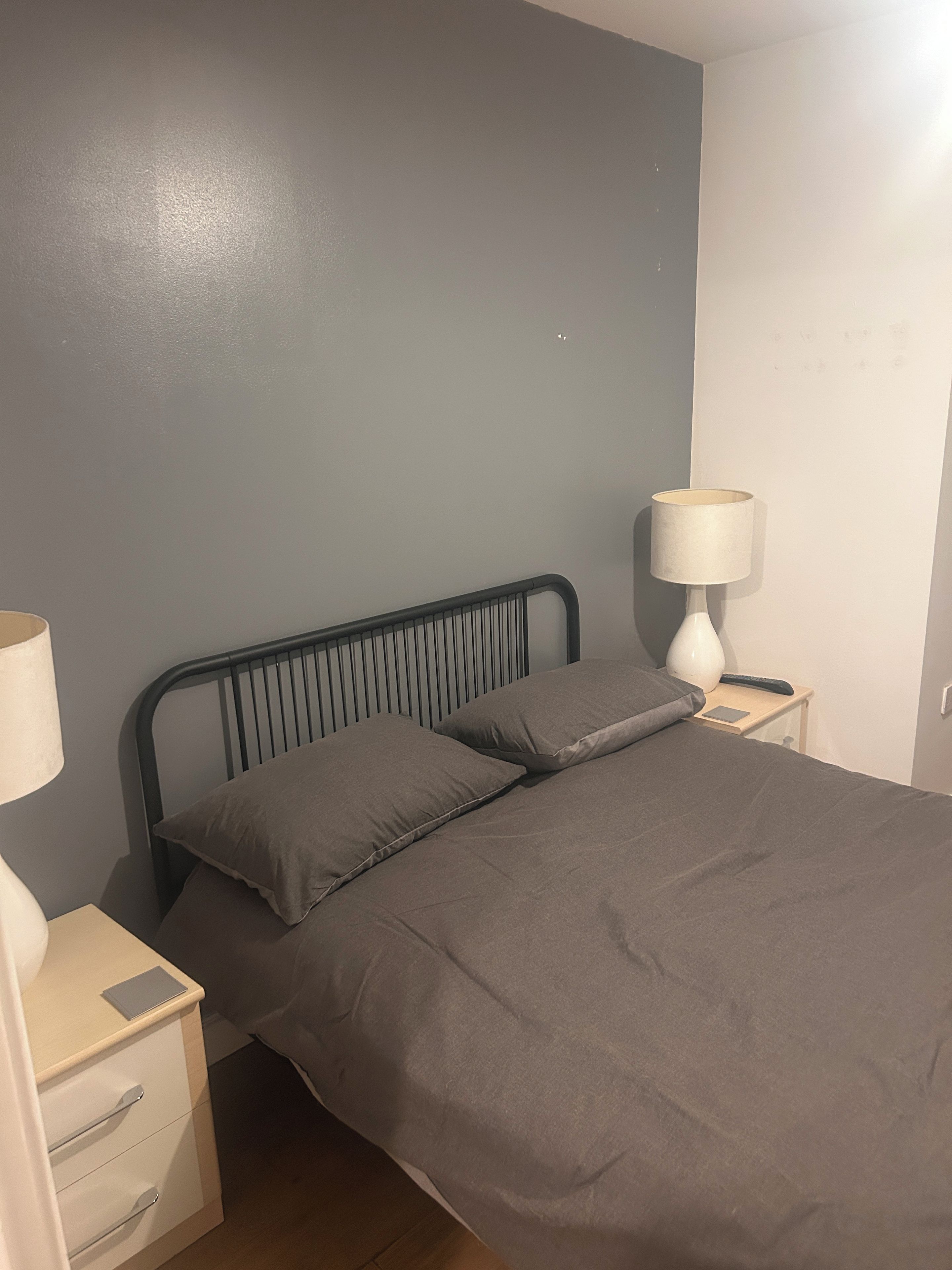 A single bed with a headboard, a bedside table with a lamp, and a nightstand with a remote control.