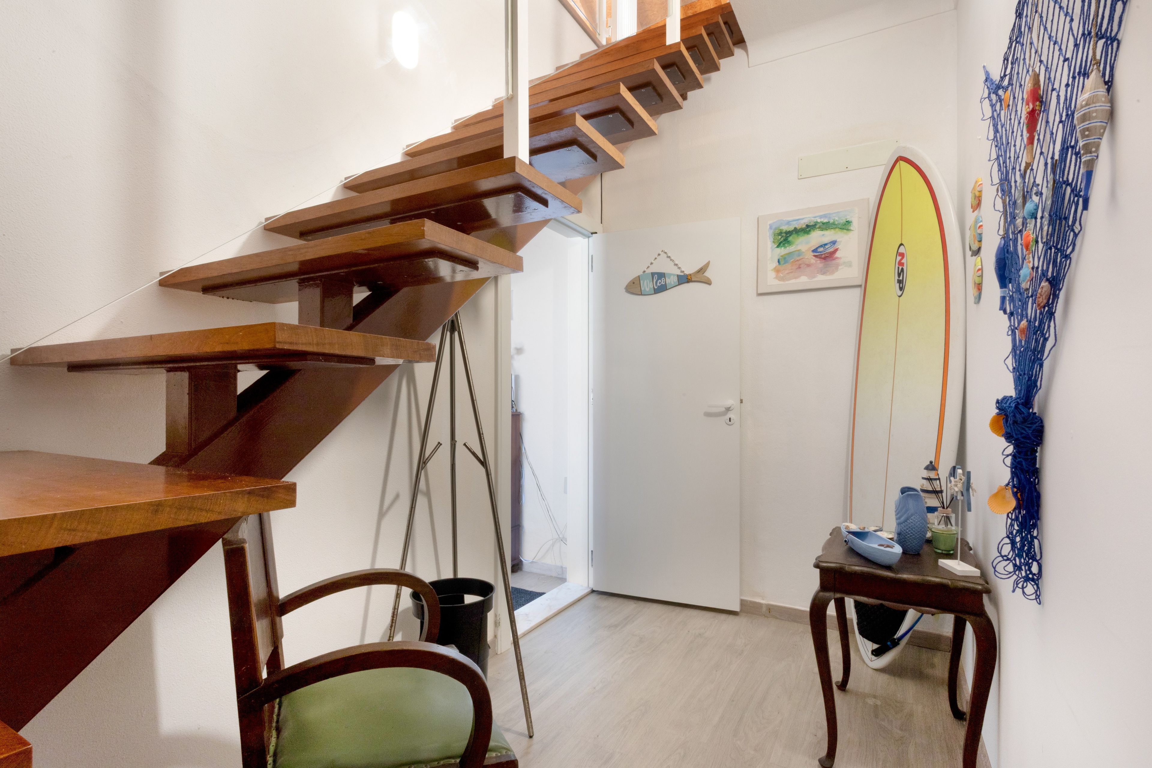 Een houten trap die leidt naar een kamer met een surfboard decoratie, een kleine tafel met een blauwe kom en een stoel.