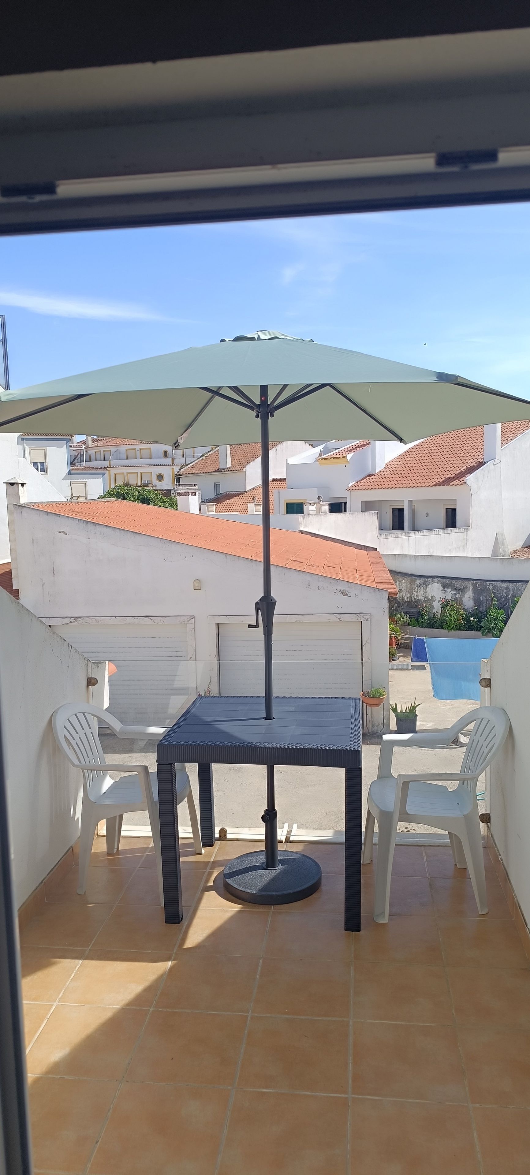 Un balcón con una mesa y sillas, vistas a edificios y una montaña al fondo.
