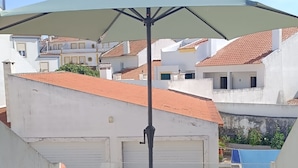 A balcony with a table and chairs, a view of buildings, and a mountain in the background. - 'Waves Inn' Surf, Beach & Relax. With Wi-Fi (Silveira)