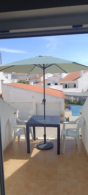 Un balcón con una mesa y sillas, vistas a edificios y una montaña al fondo.