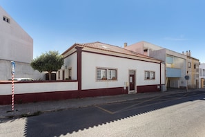 A two-story building with a red and white facade, a tiled roof, and a small tree in front.