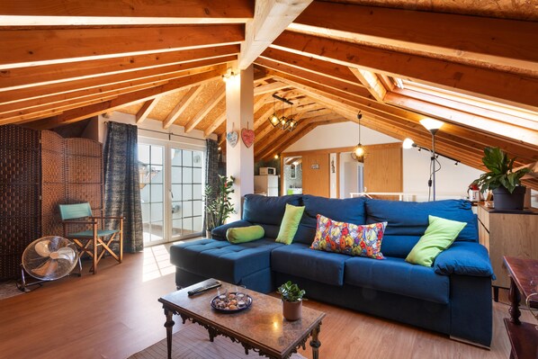 A cozy living room with a blue sectional sofa, a wooden ceiling, and a large window.