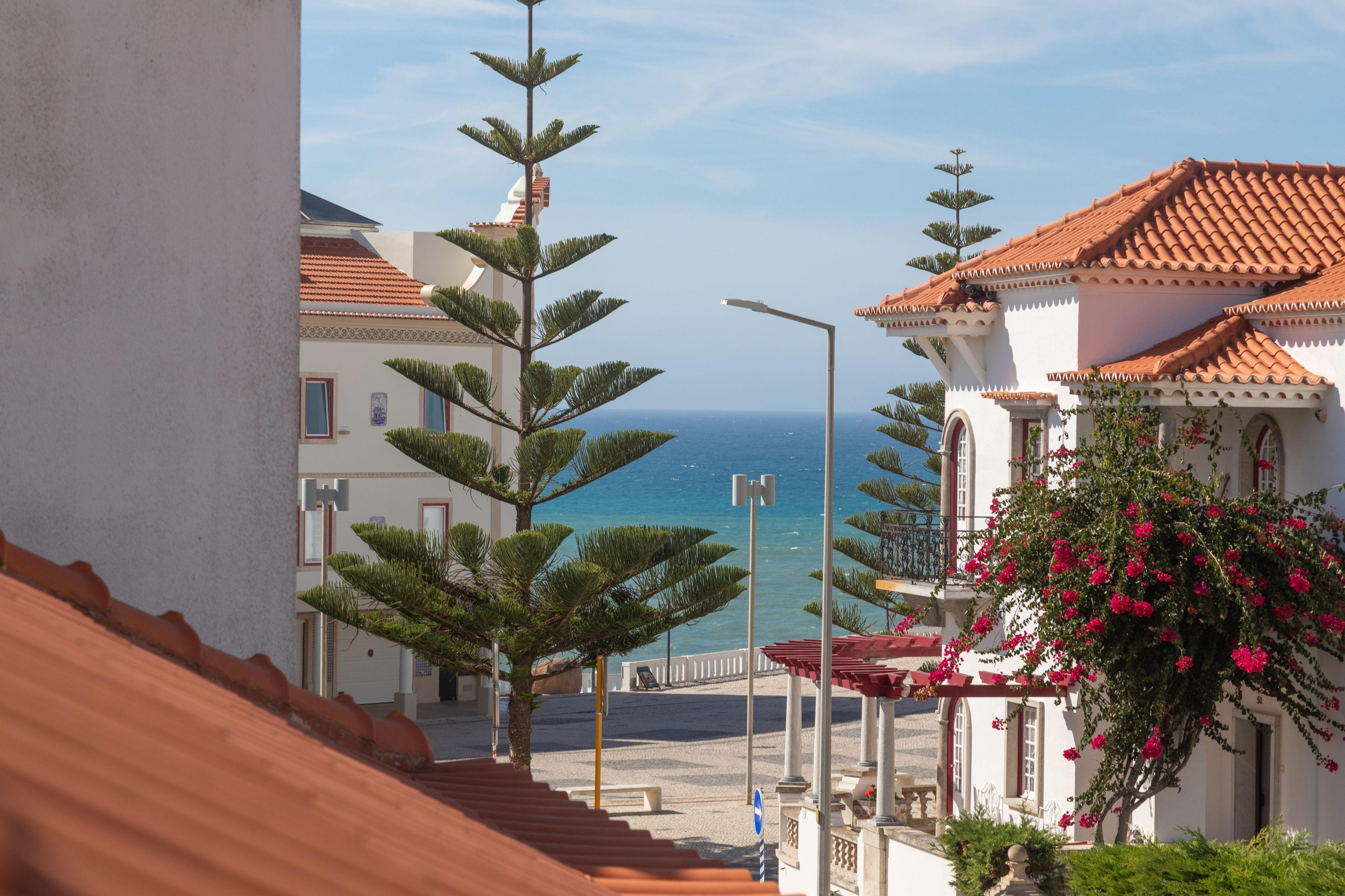 Uma rua costeira com edifícios, céu claro e vista para o mar.