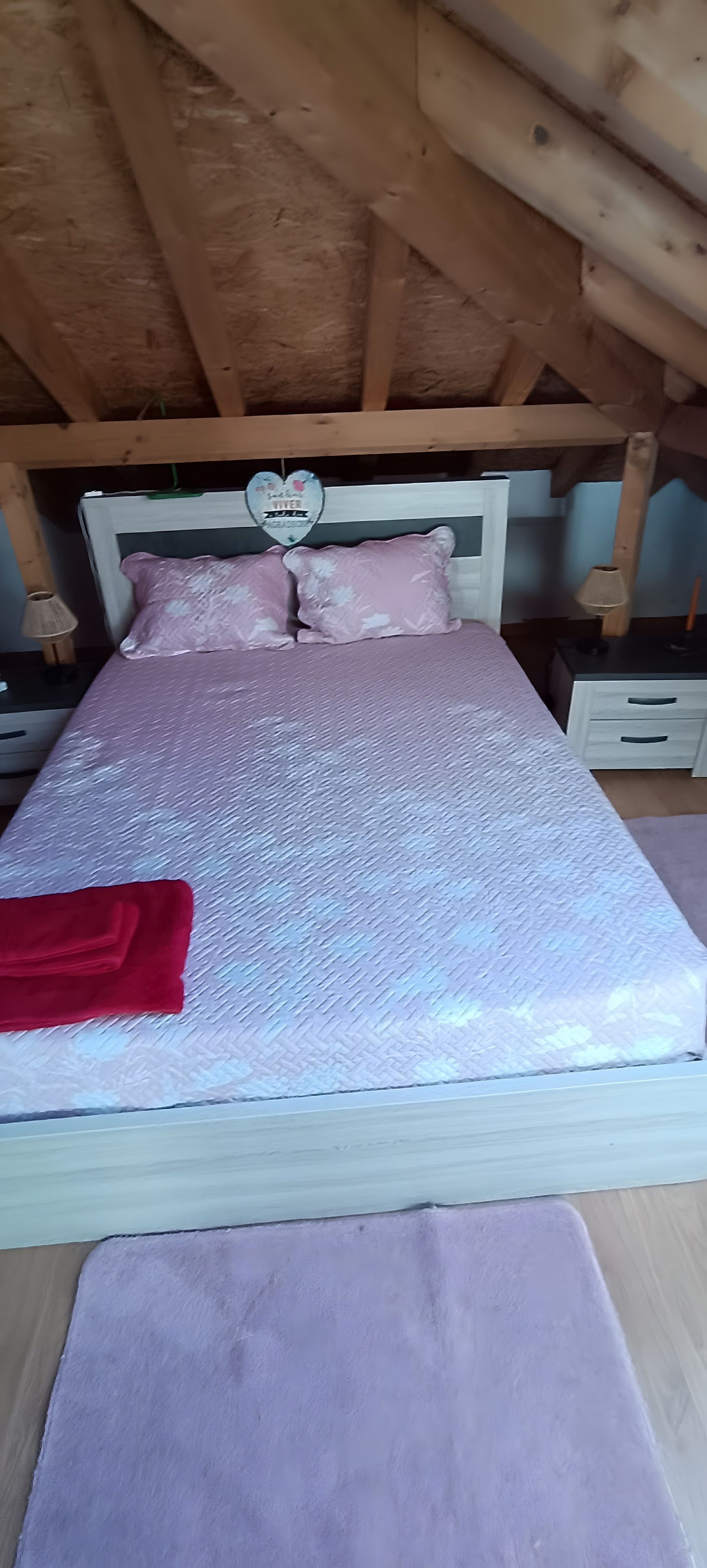 Una cama con un colchón blanco texturizado, almohadas rosadas y una manta roja.
