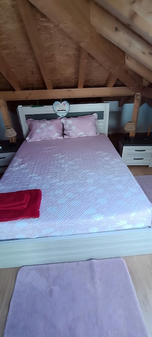 Una cama con un colchón blanco texturizado, almohadas rosadas y una manta roja.