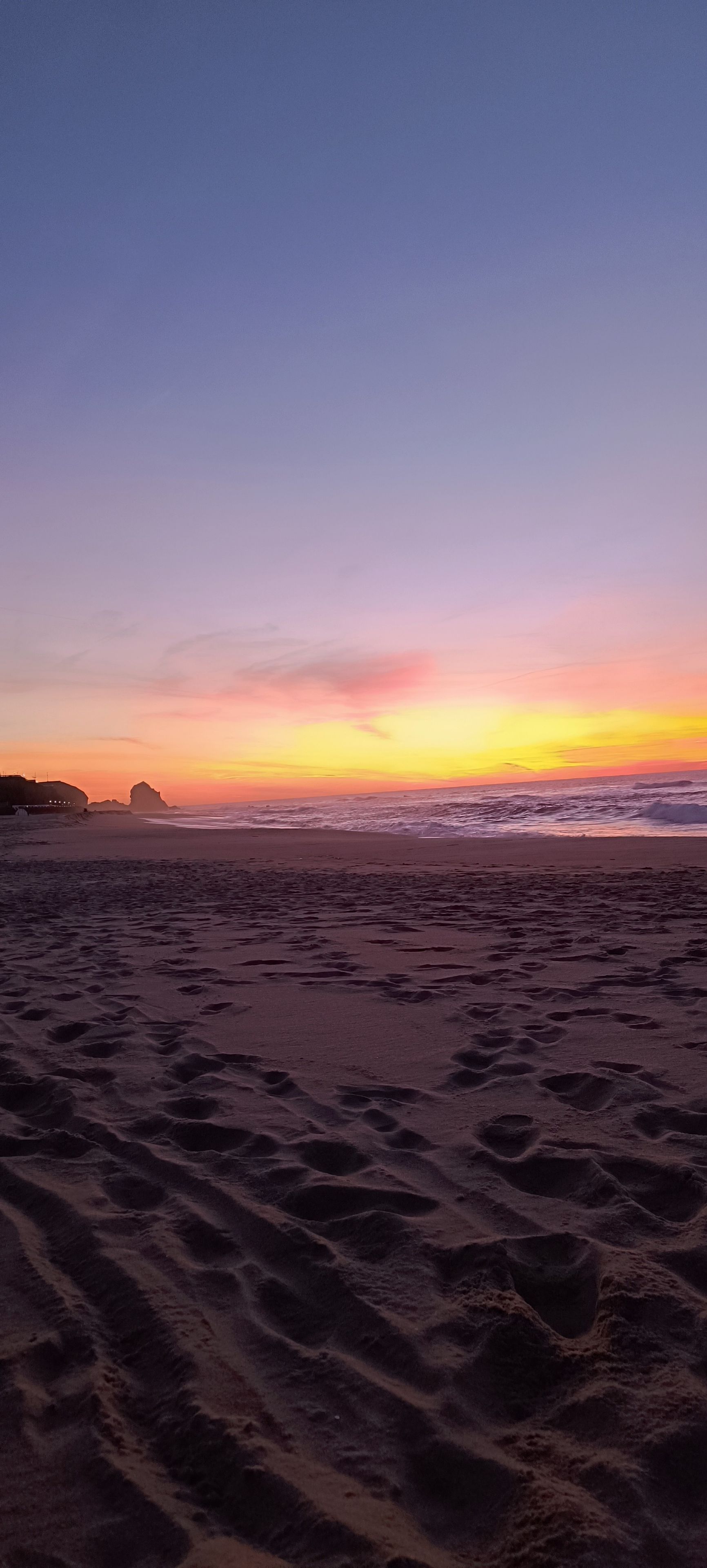 A beach with footprints in the sand and a sunset in the background.