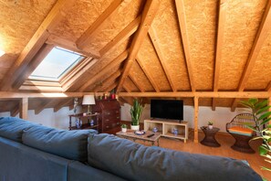 A cozy attic room with a sloped wooden ceiling, a sofa, a television, and various decorative items.