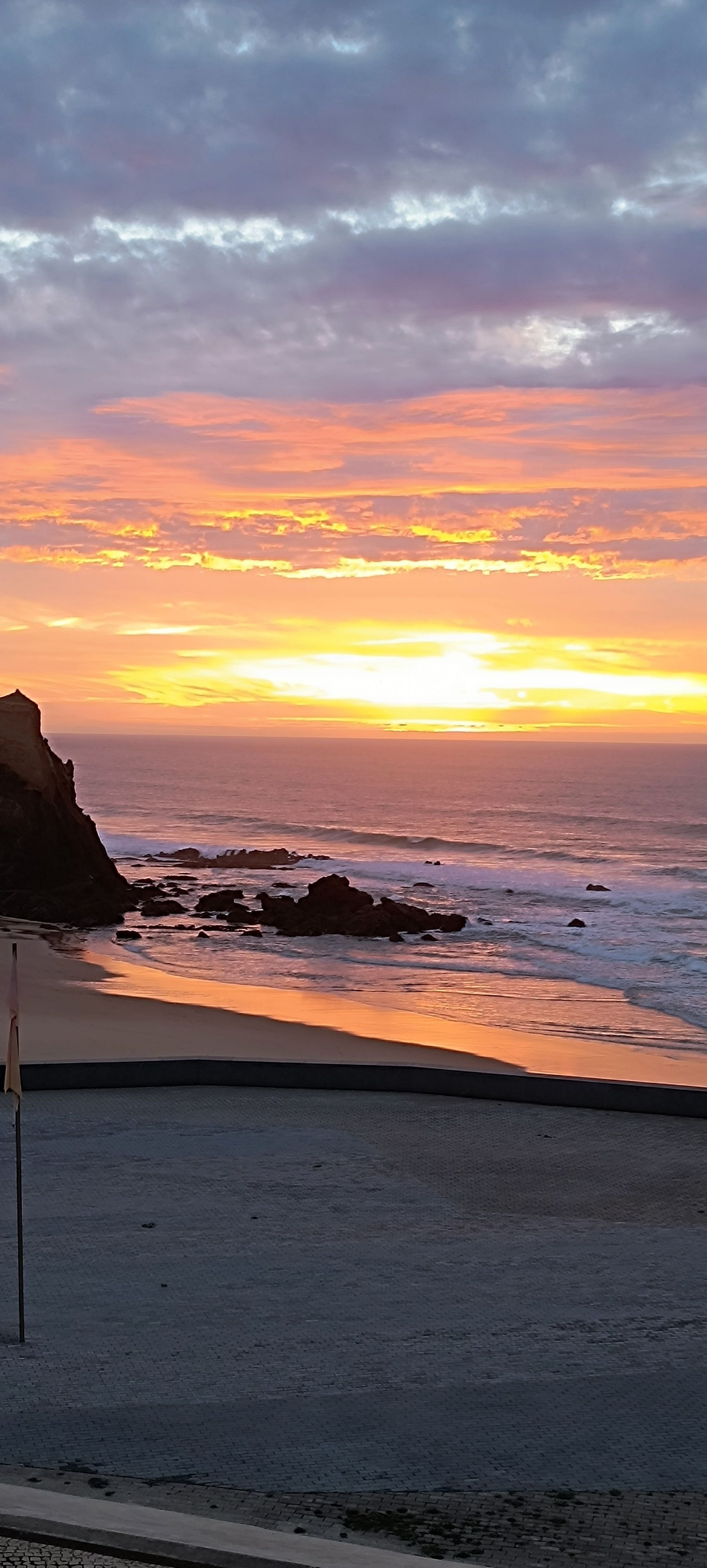 Uma praia com um pôr do sol, costa rochosa e céu limpo.