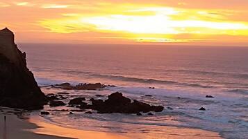 Uma praia com um pôr do sol, costa rochosa e céu limpo.