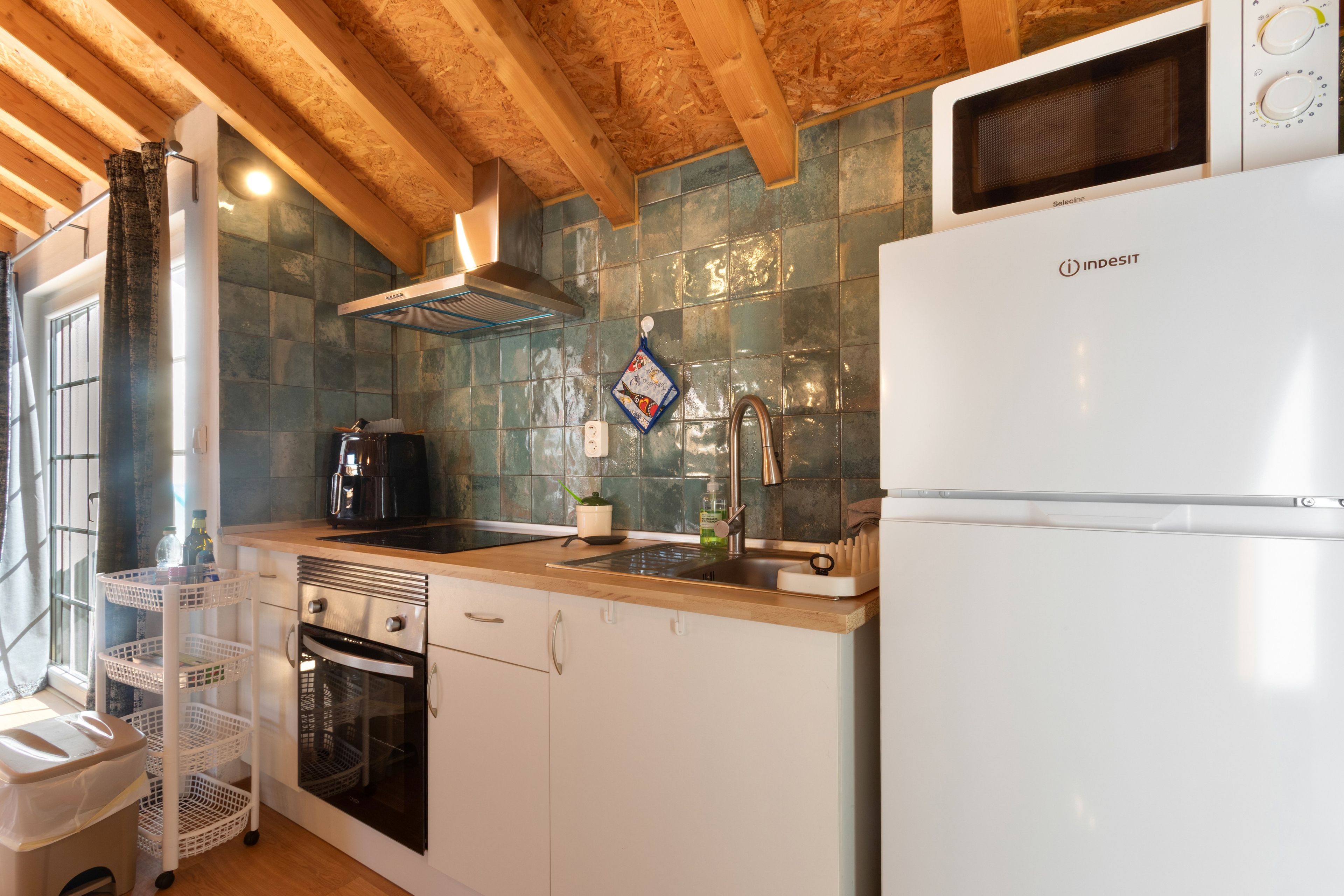 Una cocina compacta con horno empotrado, campana extractora de acero inoxidable y refrigerador blanco.