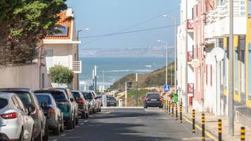 A coastal street lined with parked cars and buildings, leading towards the sea.