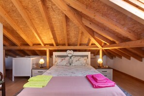 A bedroom with a sloped ceiling, wooden beams, a bed with floral bedding, two bedside lamps, and a radiator.