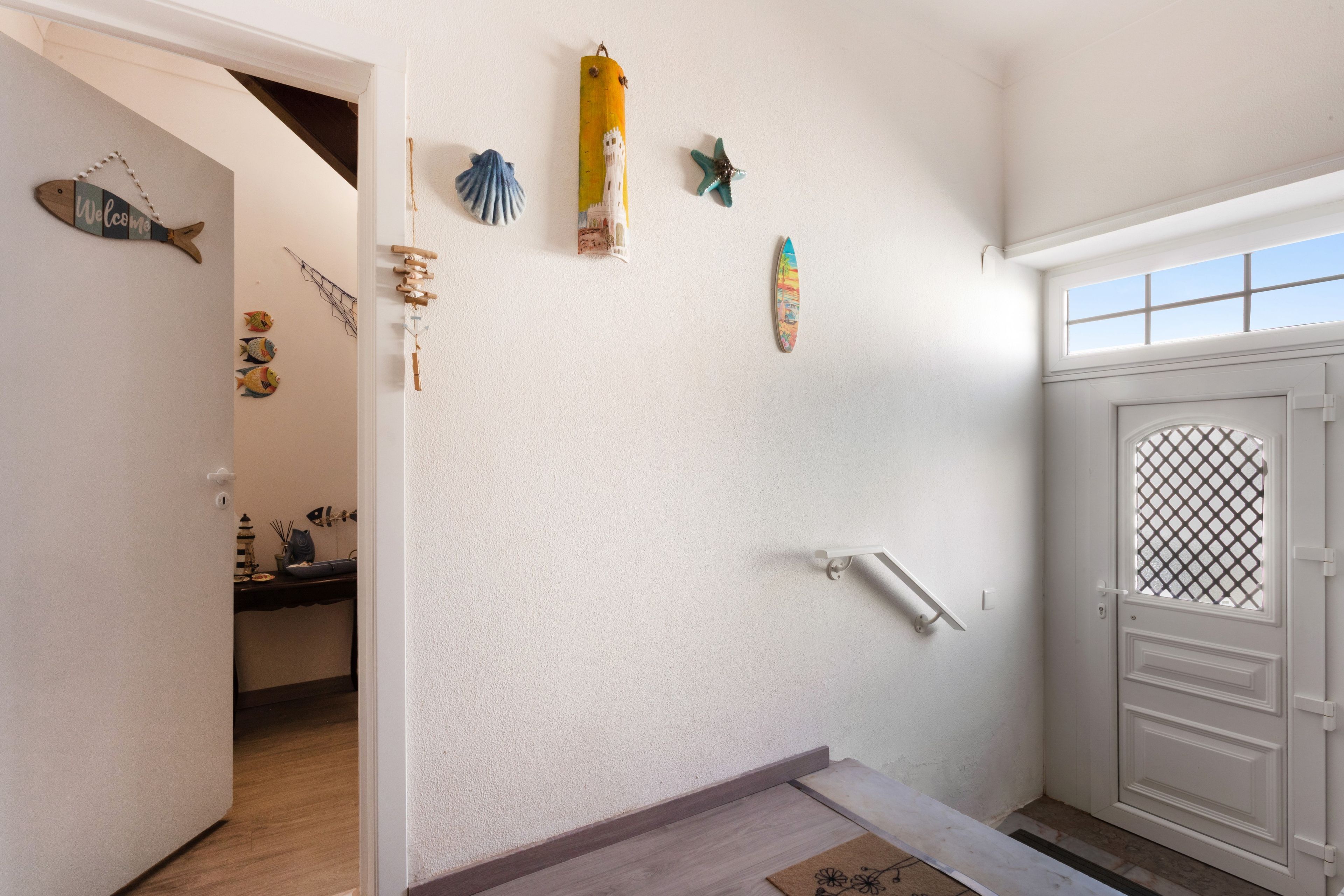 Um corredor com porta branca, piso de madeira e decorações na parede, incluindo uma prancha de surf, um peixe e um farol.