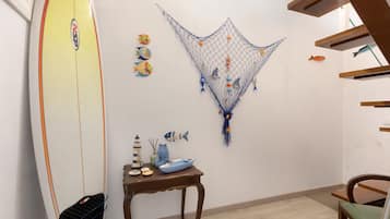 Ein Zimmer mit einem an der Wand liegenden Surfbrett, einem kleinen Tisch mit Dekoration und einer Wandgestaltung mit Fischen und Fischernetzen.