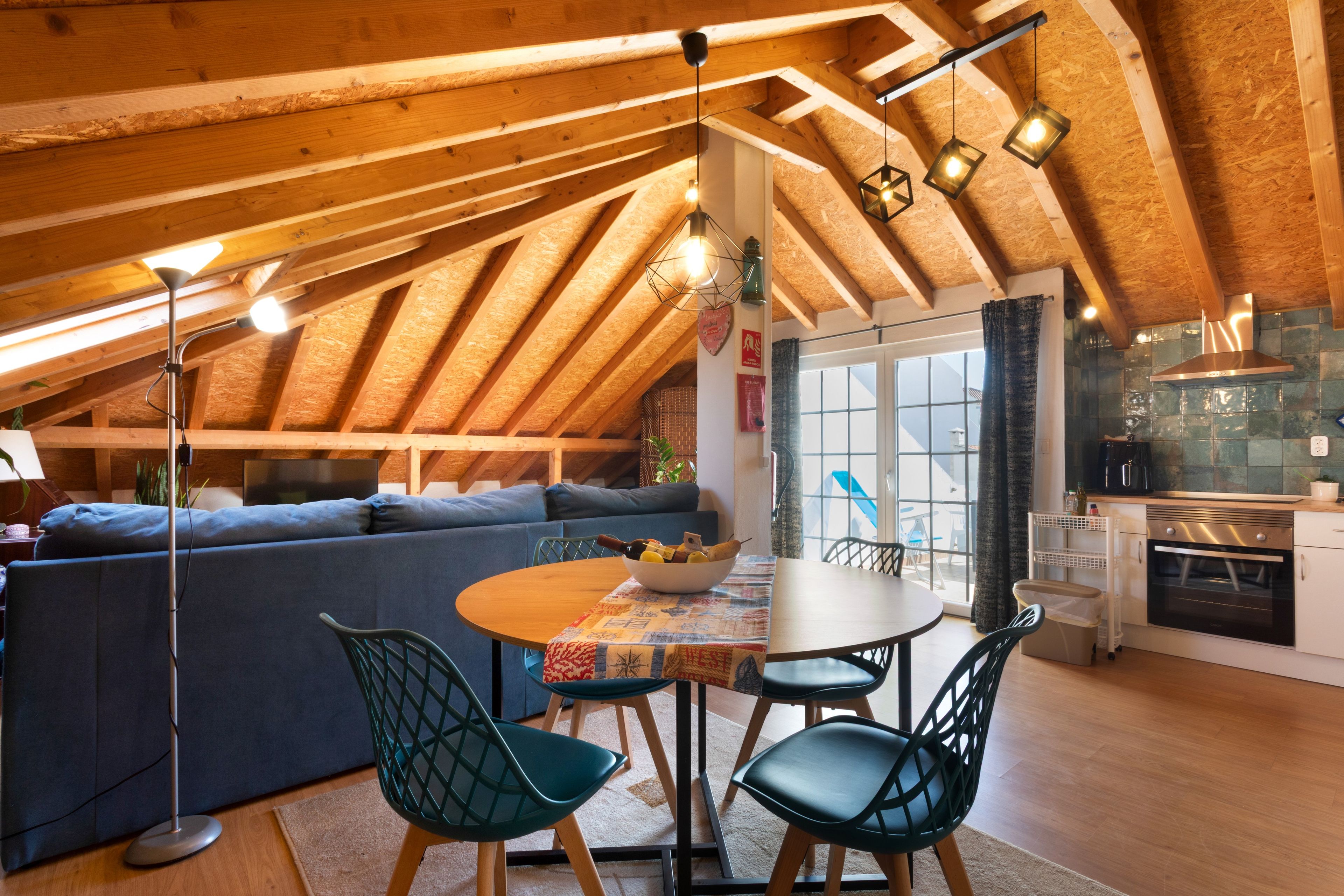 Een knus loft-appartement met een hoge plafond, een eethoek met tafel en stoelen, een bank en een keuken met fornuis en kasten.