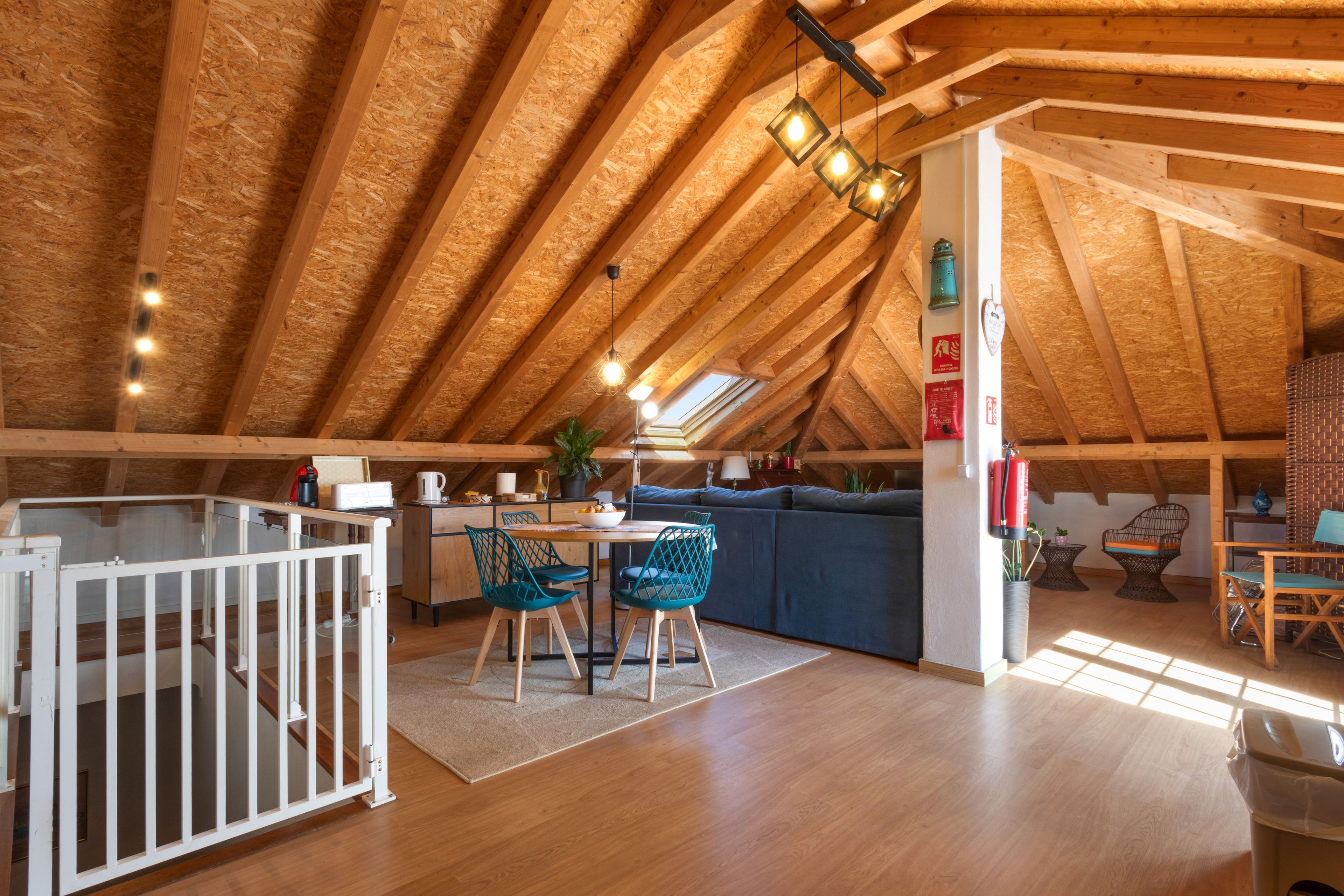 Una habitación acogedora en el ático con un alto techo de madera, un comedor con mesa y sillas, una zona de cocina y un pequeño rincón de descanso con un sofá y sillas.