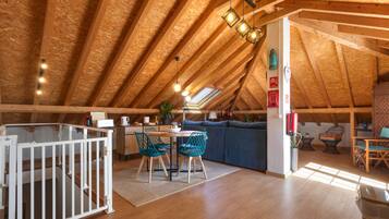 Una habitación acogedora en el ático con un alto techo de madera, un comedor con mesa y sillas, una zona de cocina y un pequeño rincón de descanso con un sofá y sillas.