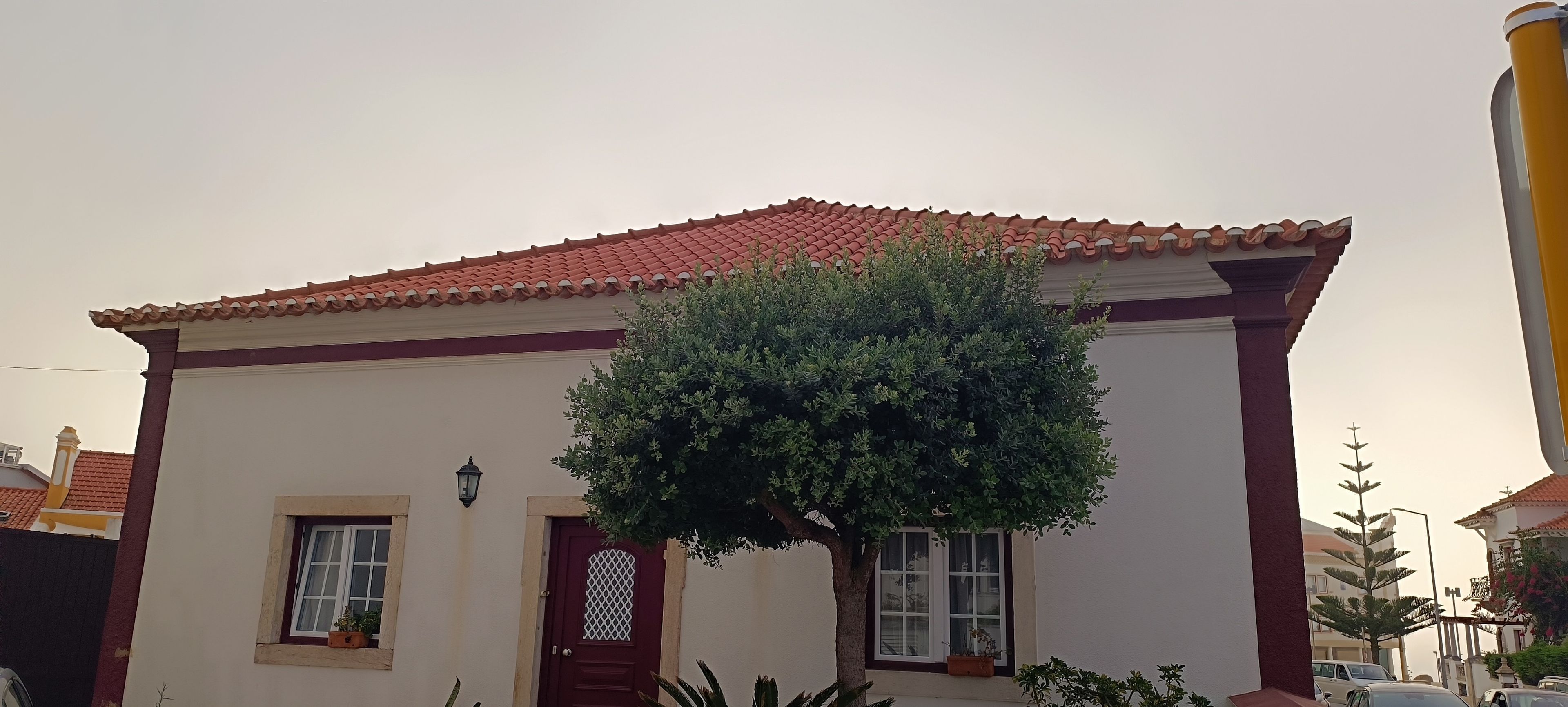 Un edificio con techo de tejas rojas, fachada blanca y un árbol en primer plano.