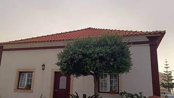Un edificio con techo de tejas rojas, fachada blanca y un árbol en primer plano.
