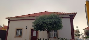 Un edificio con techo de tejas rojas, fachada blanca y un árbol en primer plano.
