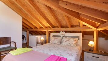 Quarto com teto de madeira, cama com roupa de cama florida, duas luminárias de apoio e decoração em formato de coração na cabeceira.
