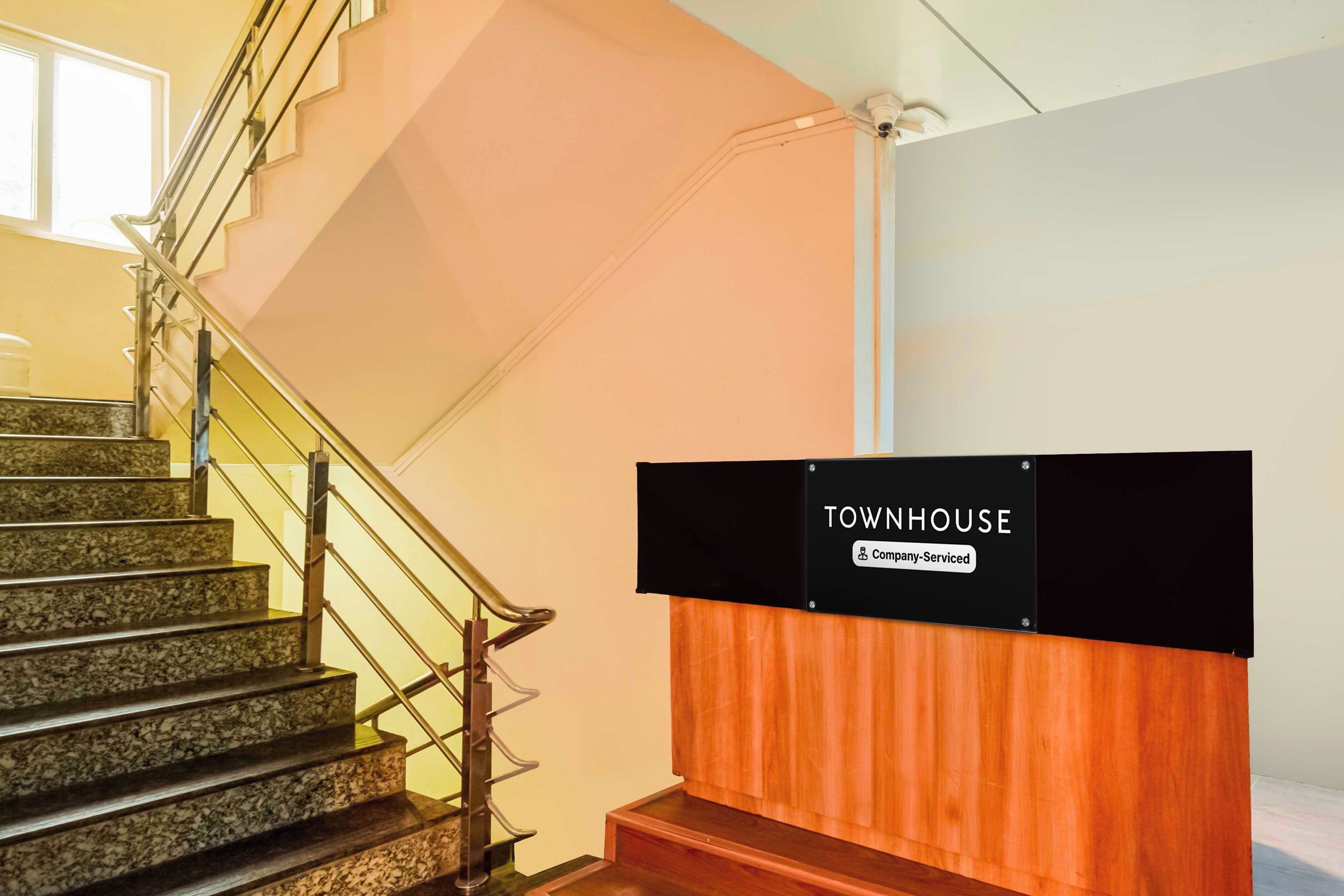 Una escalera con barandilla, un cartel que indica 'TOWNHOUSE Company-Serviced' y un panel de madera.