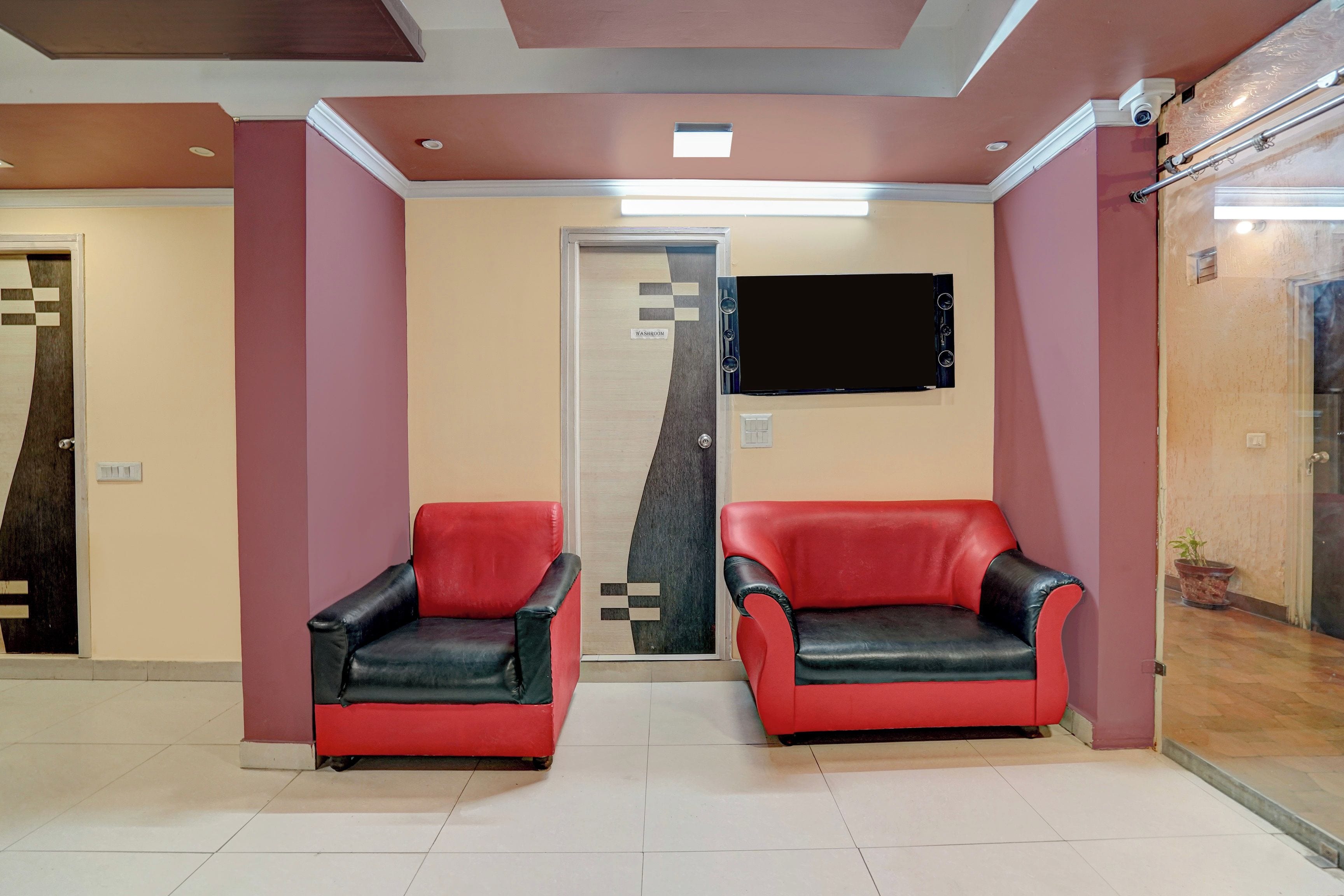 Un área de recepción con dos sillas rojas y negras, un televisor de pantalla plana en la pared y una puerta con la leyenda 'WASHROOM'.