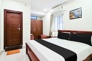 Una habitación de hotel con una cama, un armario, un ventanal con cortinas, un cuadro en la pared y una mesita con una lámpara.