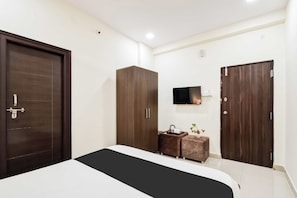 Un dormitorio con cama, armario, televisor y una mesita con una planta.