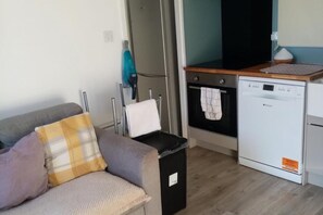 A compact living space with a sofa, a small trash bin, a washing machine, and a kitchenette area.