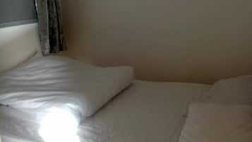 Een bed met witte beddengoed en een hoofdbord, met een gordijn gedeeltelijk zichtbaar aan de linkerkant.