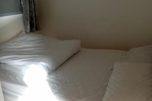 A bed with white bedding and a headboard, with a curtain partially visible on the left.