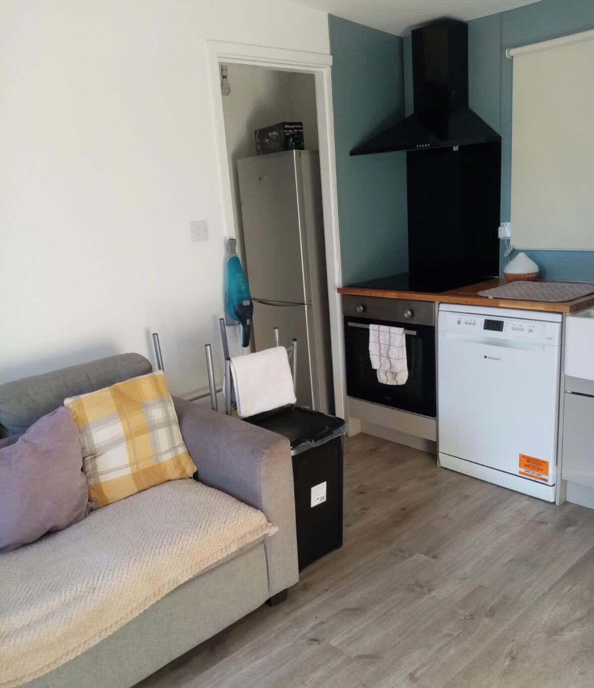 A compact living space with a kitchenette, a sofa with cushions, a trash bin, and a washing machine.