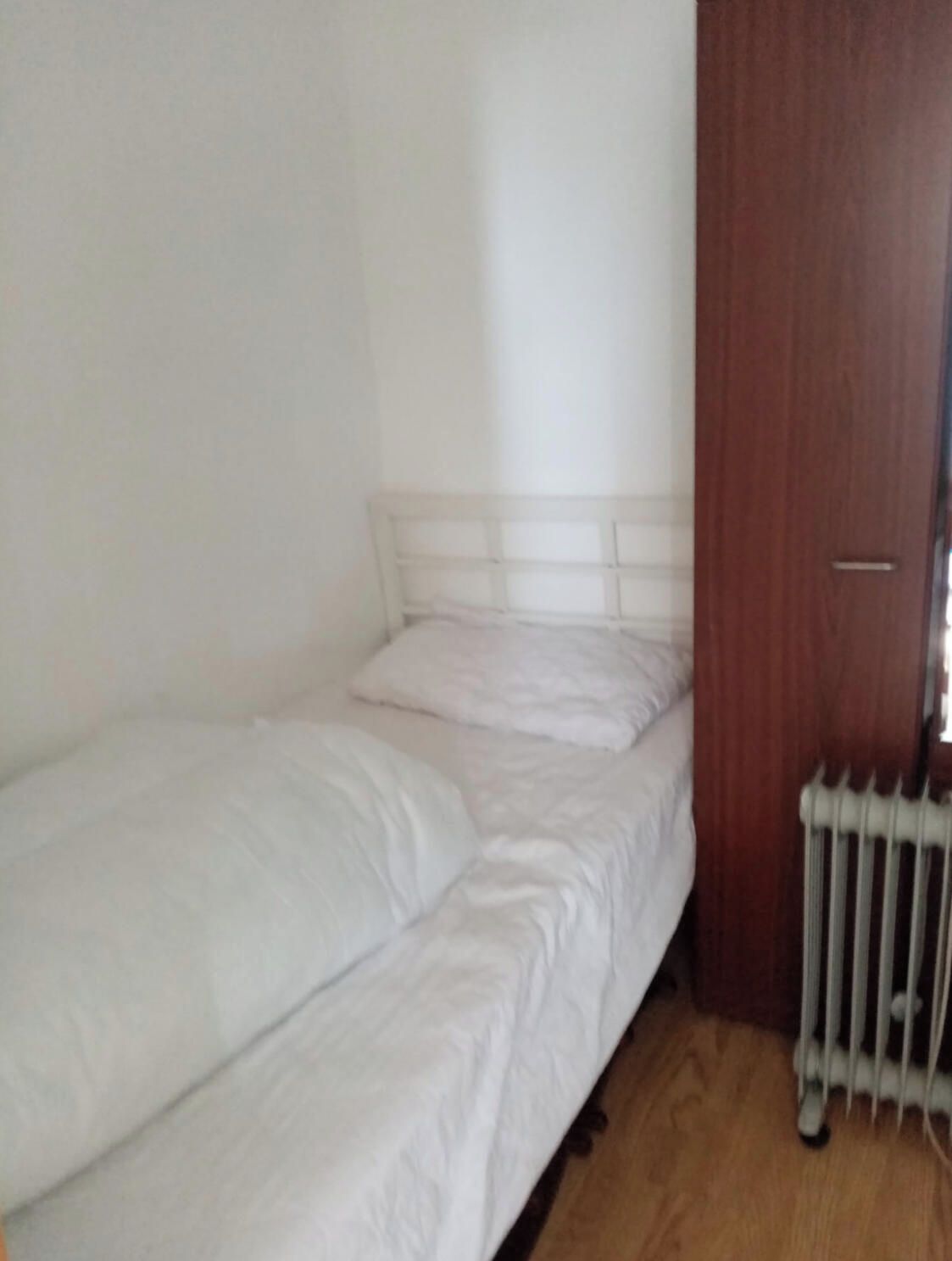 A single bed with a wooden headboard in a room with a radiator and a wooden door.