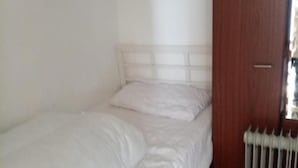 A small, single-bed room with a white headboard and a wooden door.