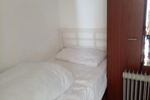 A small, single-bed room with a white headboard and a wooden door.