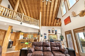 A spacious living area with a high ceiling, wooden beams, a leather sofa, and a dining area with wooden cabinets. - Beautiful Lakefront Cabin with Private Dock near Yellowstone in Island Park, Idaho (Island Park)
