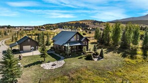A large log cabin with a metal roof, surrounded by a stone patio and a small fire pit. - Beautiful Lakefront Cabin with Private Dock near Yellowstone in Island Park, Idaho (Island Park)