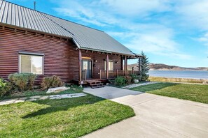 A wooden cabin with a porch, a front door, and a view of a lake. - Beautiful Lakefront Cabin with Private Dock near Yellowstone in Island Park, Idaho (Island Park)